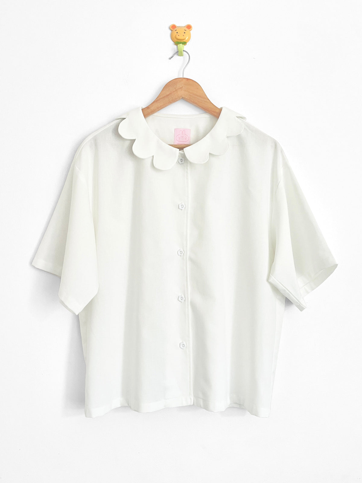 White blouse with a collar on a wooden hanger against a white background