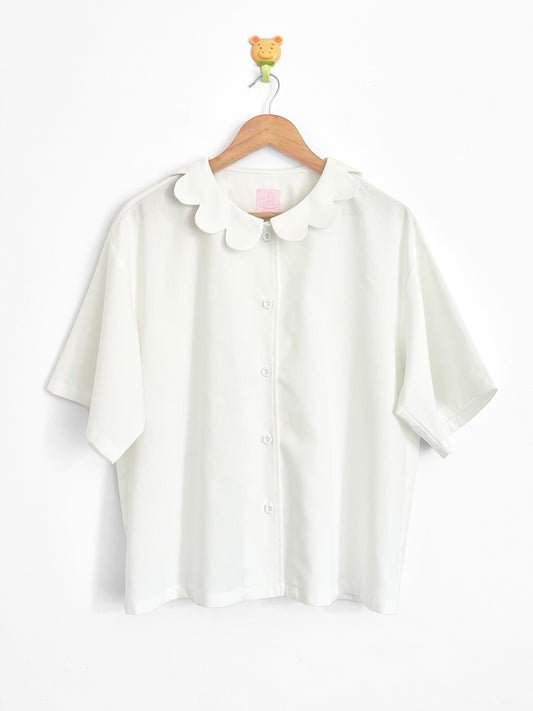 White blouse with a collar on a wooden hanger against a white background