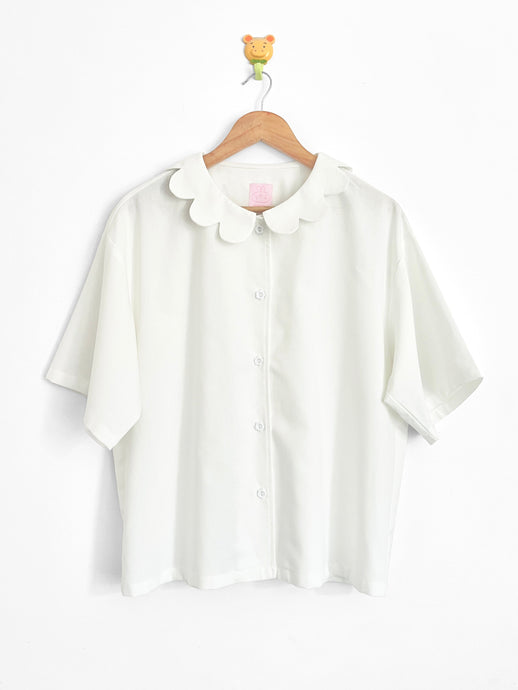 White blouse with a collar on a wooden hanger against a white background